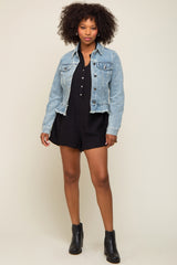 woman wearing a light wash denim jacket over a black romper with buttons and ankle boots