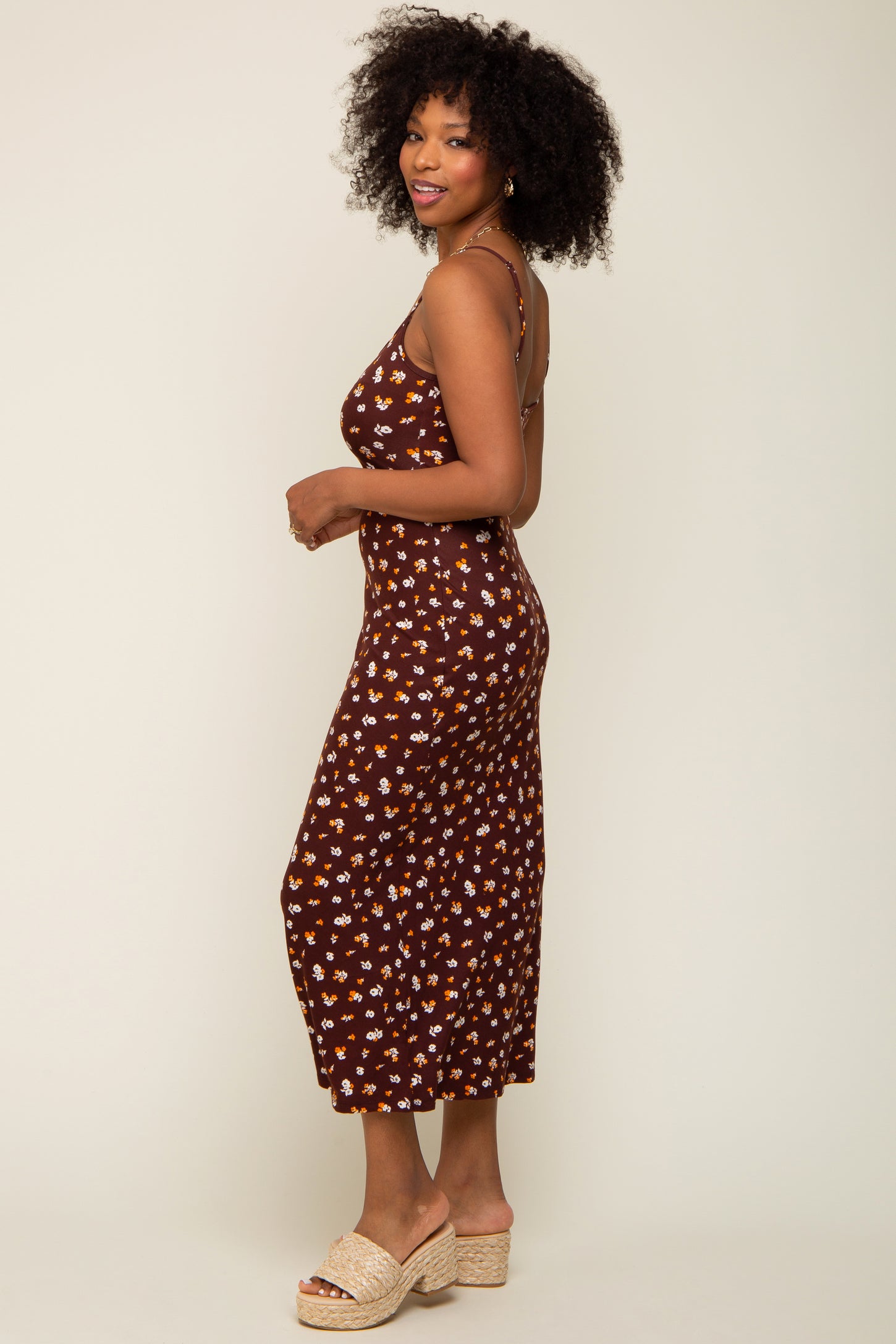 Woman with curly hair wearing a brown floral midi dress and platform sandals against a neutral background