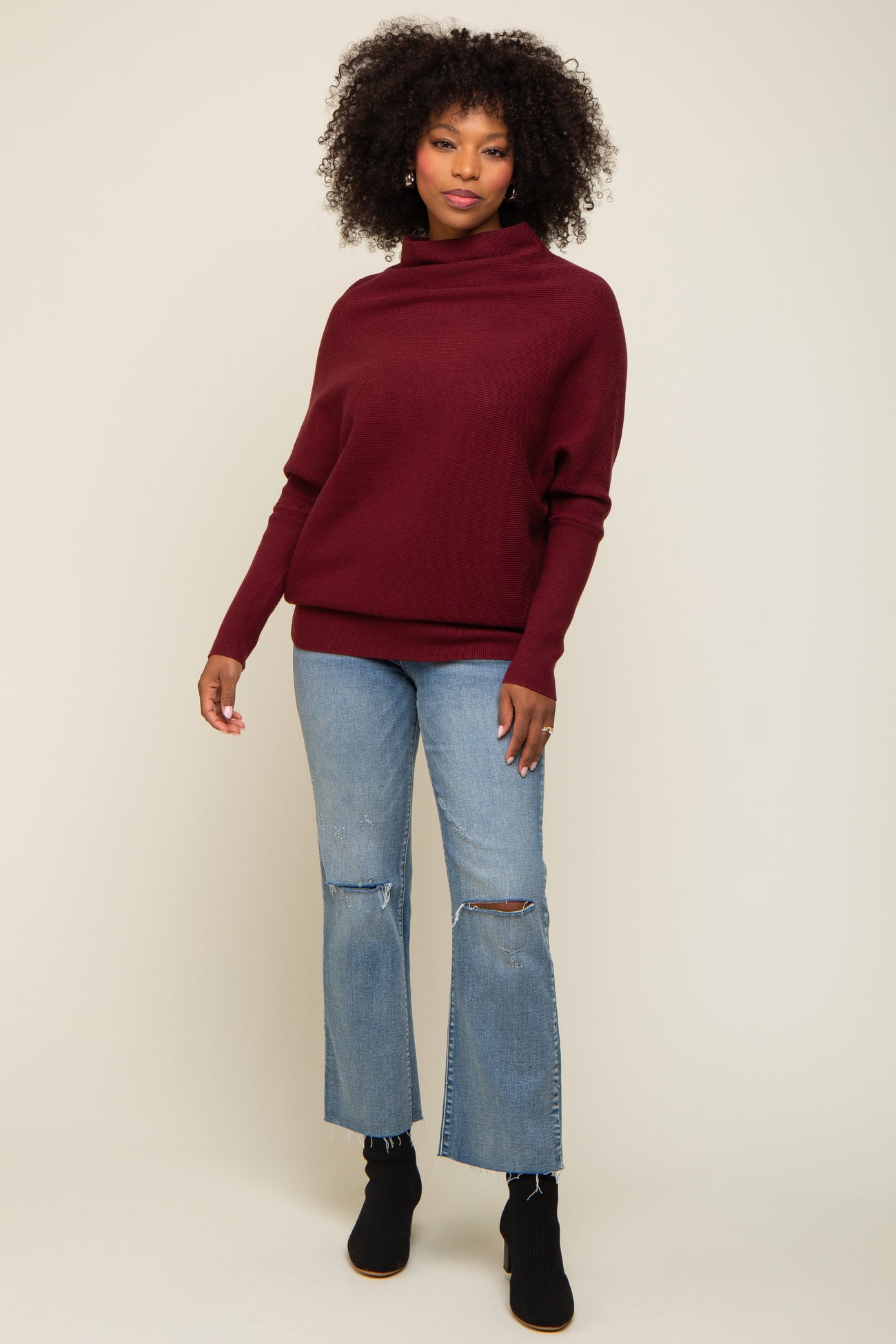 woman wearing a burgundy cozy sweater with a high neckline and light blue distressed flared jeans