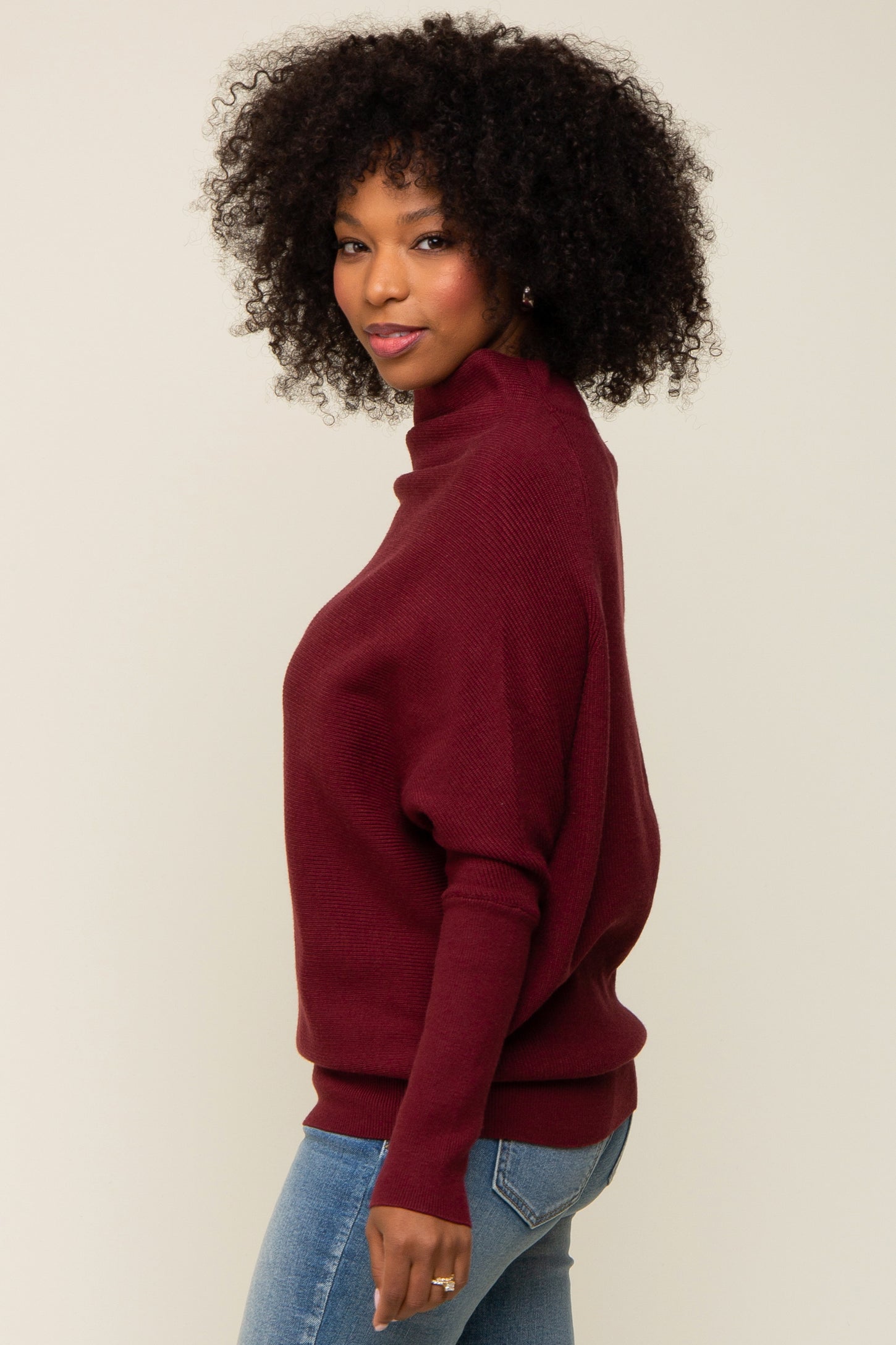 woman wearing a burgundy high-neck oversized sweater with dropped shoulders and slim-fit jeans