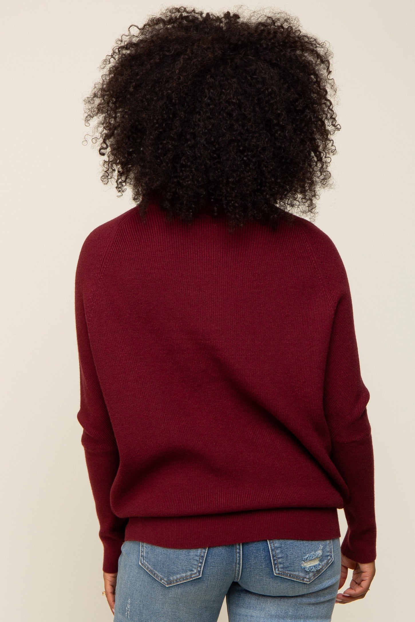 woman wearing a burgundy oversized sweater with a relaxed fit, seen from the back, paired with blue jeans