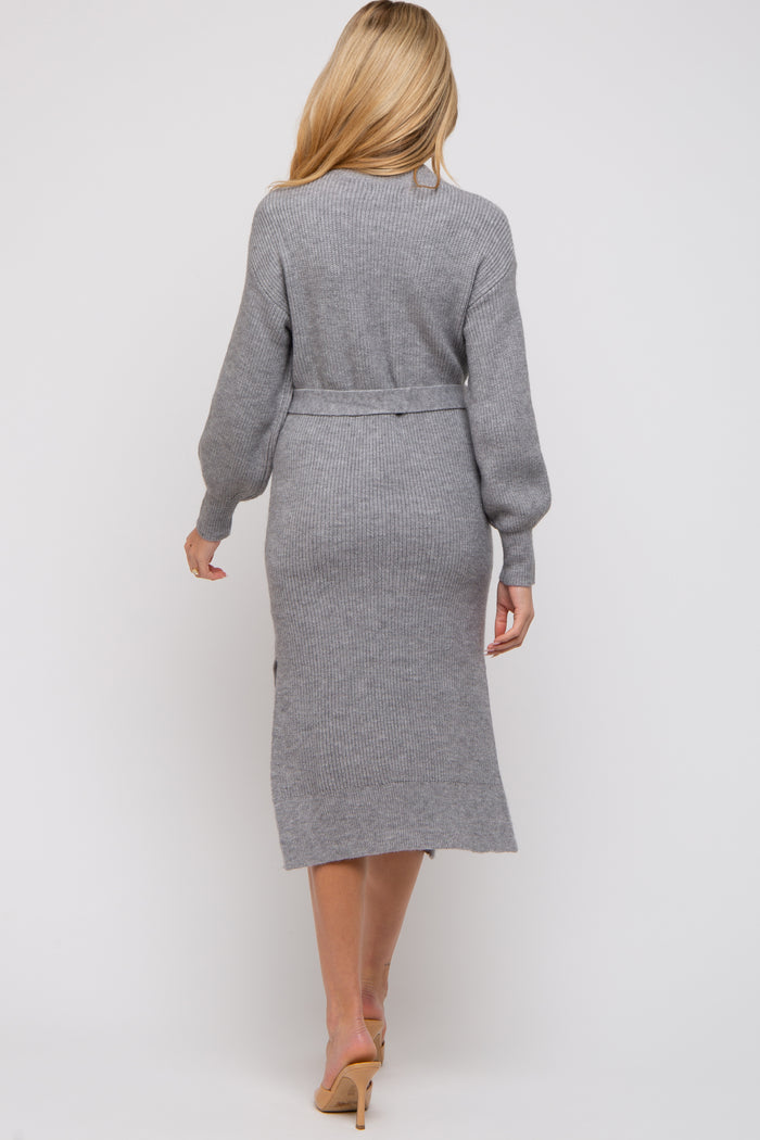 woman wearing a long grey maternity sweater dress with a belted waist, showing a subtle slit at the back