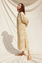 woman wearing a loose-fitting beige patterned maxi dress with long sleeves and side slits