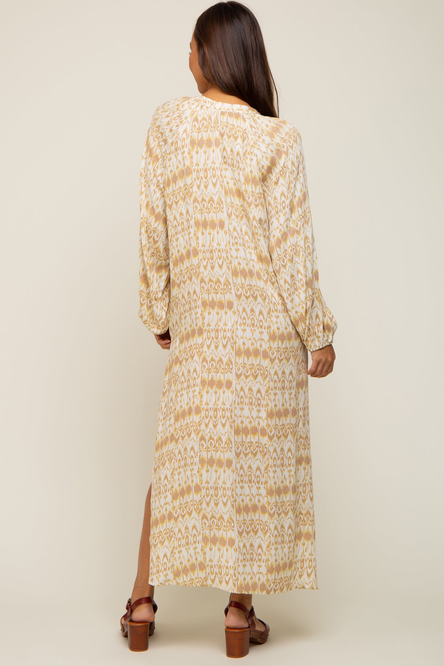 woman wearing a long sleeve beige and yellow patterned maternity dress with a side slit