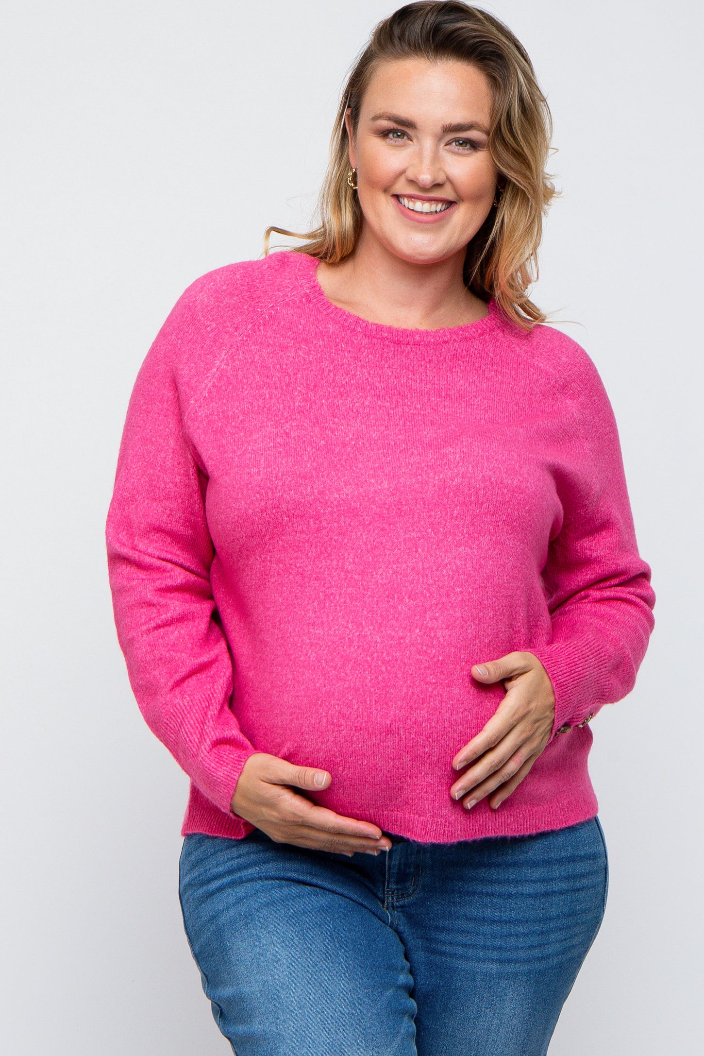 woman wearing a bright pink maternity sweater and holding her baby bump, paired with blue jeans