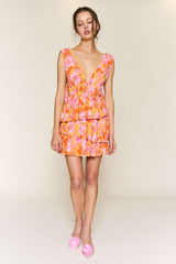 woman wearing a pink and orange floral mini dress with a deep v-neck and tiered ruffles, paired with pink flats