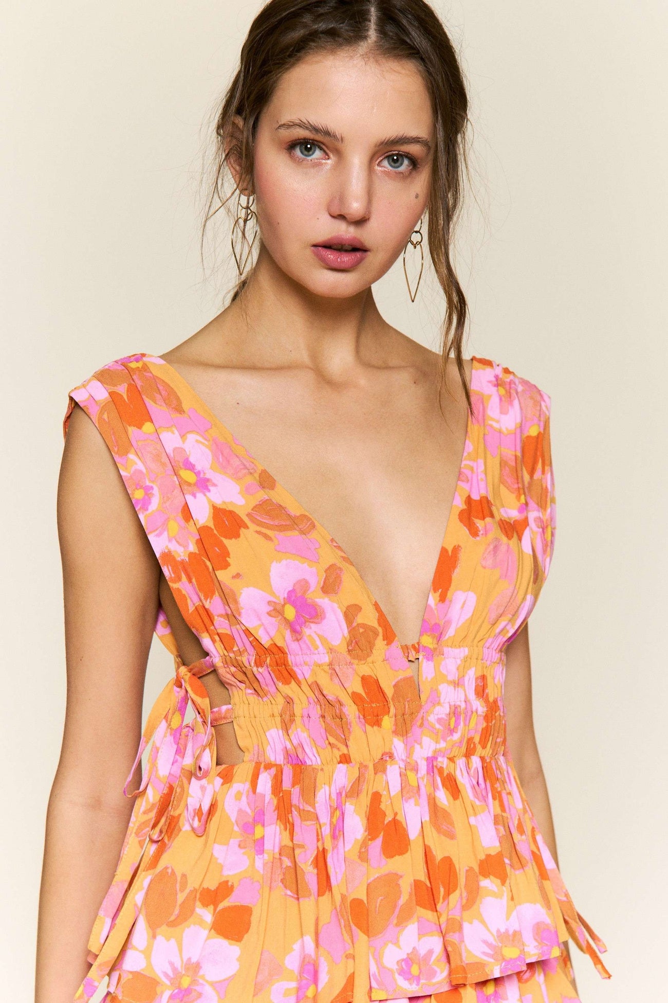 woman wearing a floral print sleeveless dress with a deep v-neckline and smocked waist in orange and pink tones