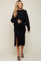 woman wearing a black maternity sweater and a black midi skirt with a slit, gently holding her baby bump