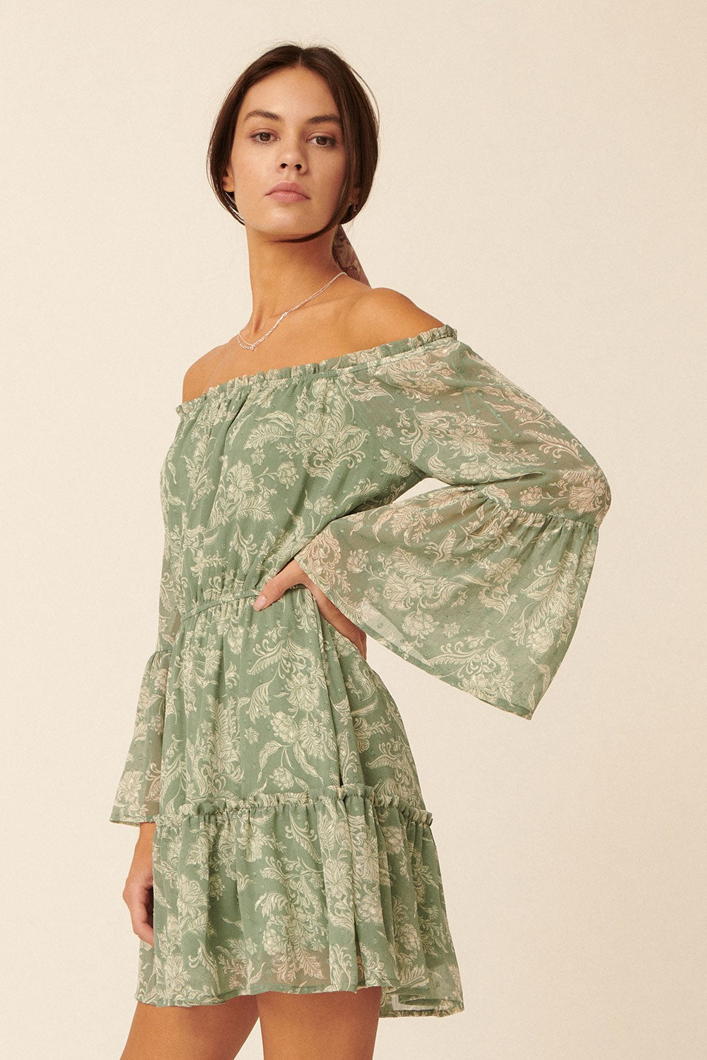 woman wearing a green floral off-the-shoulder mini dress with long bell sleeves