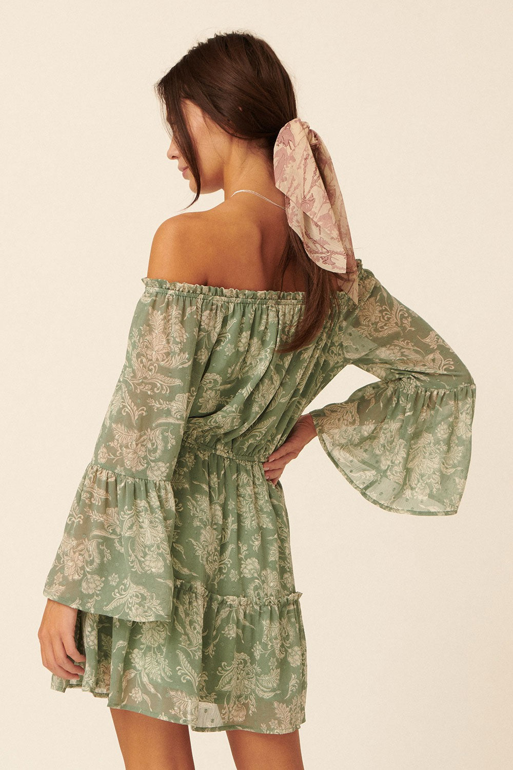 woman wearing a green off-the-shoulder dress with bell sleeves and a gathered waist, styled with a matching hair scarf