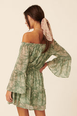 woman wearing a green off-the-shoulder dress with bell sleeves and a gathered waist, styled with a matching hair scarf