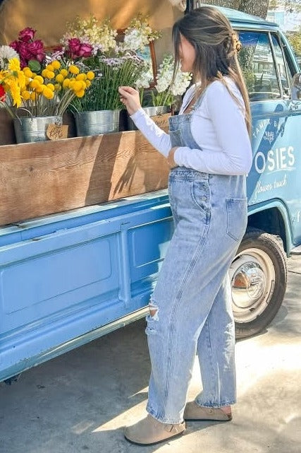 woman wearing light blue maternity overalls and a white long sleeve shirt, standing by a flower truck