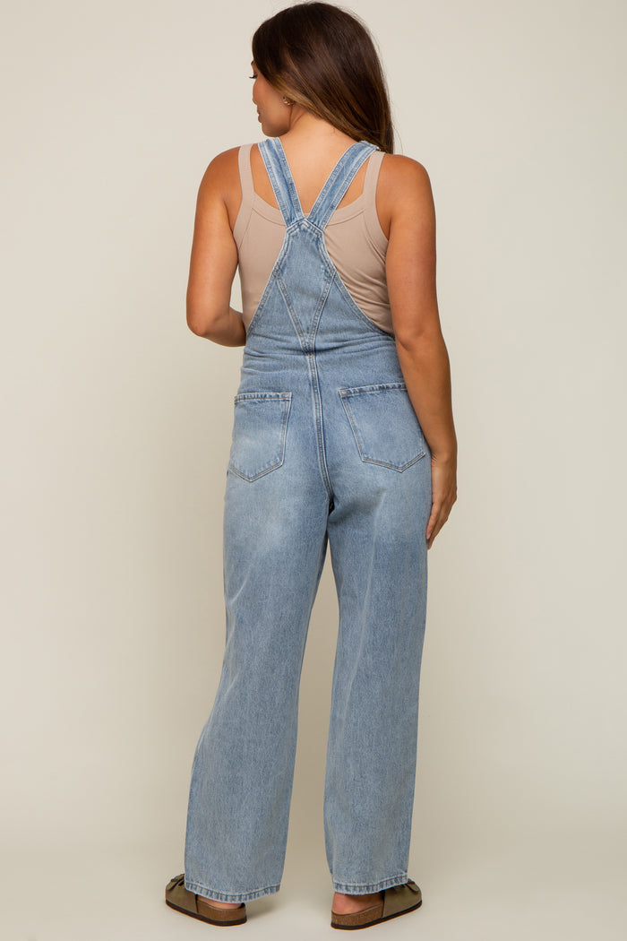 woman wearing light blue denim maternity overalls, viewed from the back, with a beige tank top underneath