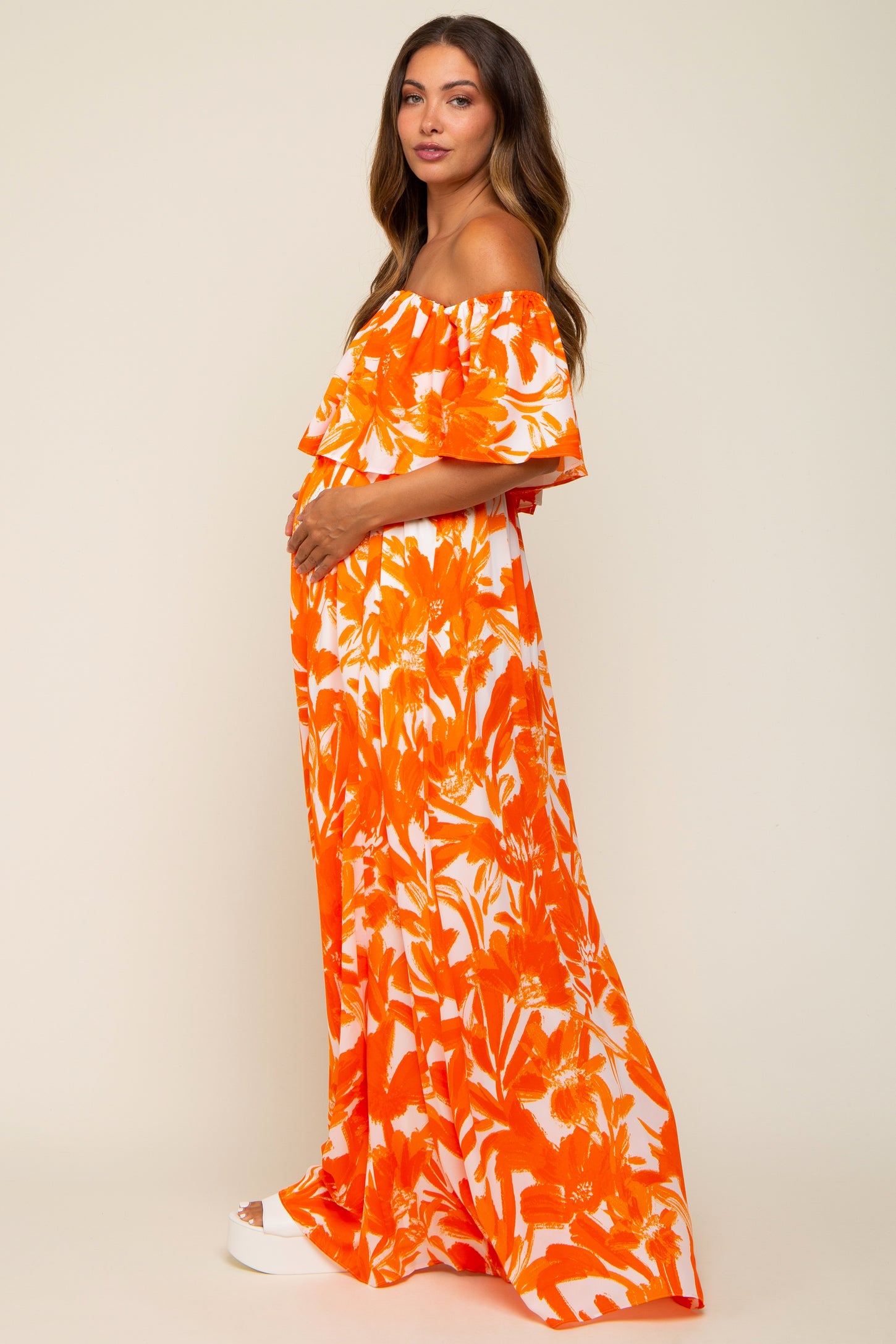 woman wearing an orange floral off-shoulder maternity dress highlighting her baby bump