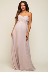 woman wearing a blush strapless maternity maxi dress with ruched bodice and flowing skirt, showcasing her baby bump