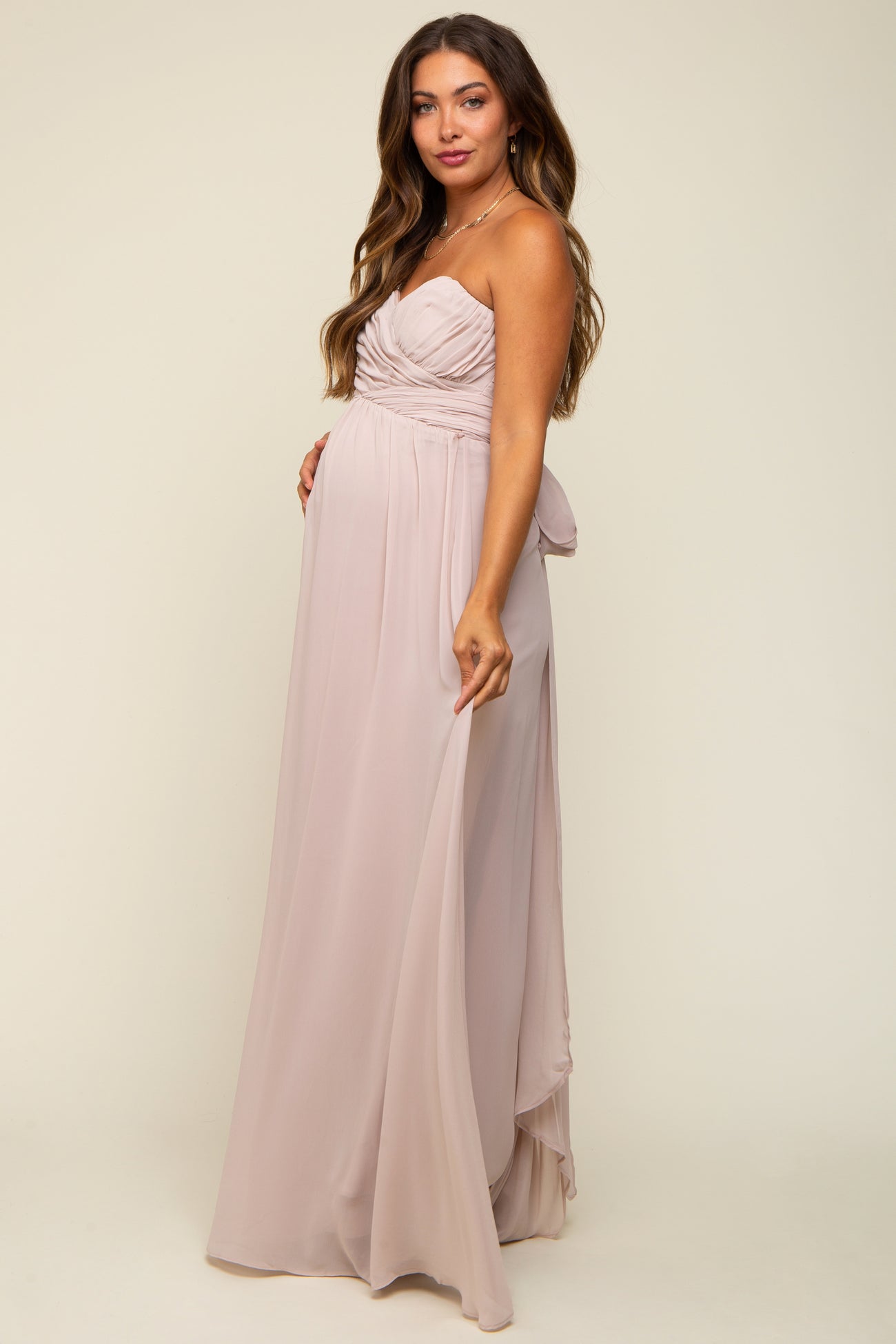 woman wearing a light pink strapless maternity gown with a ruched bodice and flowy skirt, highlighting her baby bump