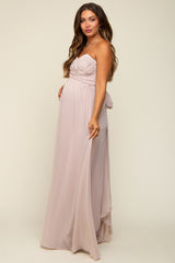 woman wearing a light pink strapless maternity gown with a ruched bodice and flowy skirt, highlighting her baby bump