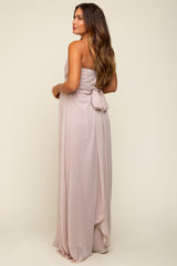 woman wearing a dusty pink strapless maternity dress with a bow detail at the back, showcasing a baby bump