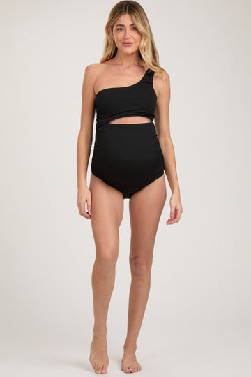 woman wearing a black one-shoulder maternity swimsuit with a cut-out detail, highlighting her baby bump