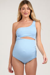 woman wearing a light blue one-shoulder maternity swimsuit with side cutout and gathered detailing, showing her baby bump