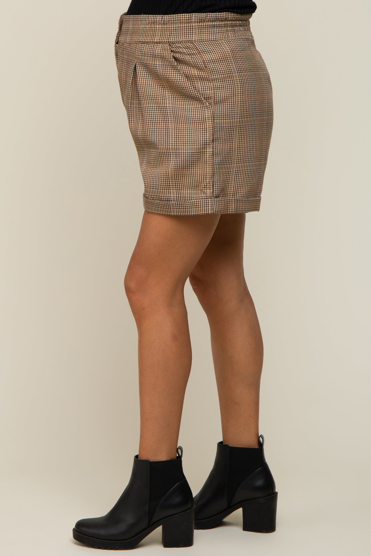 woman wearing brown plaid mini skirt and black leather ankle boots against a neutral background