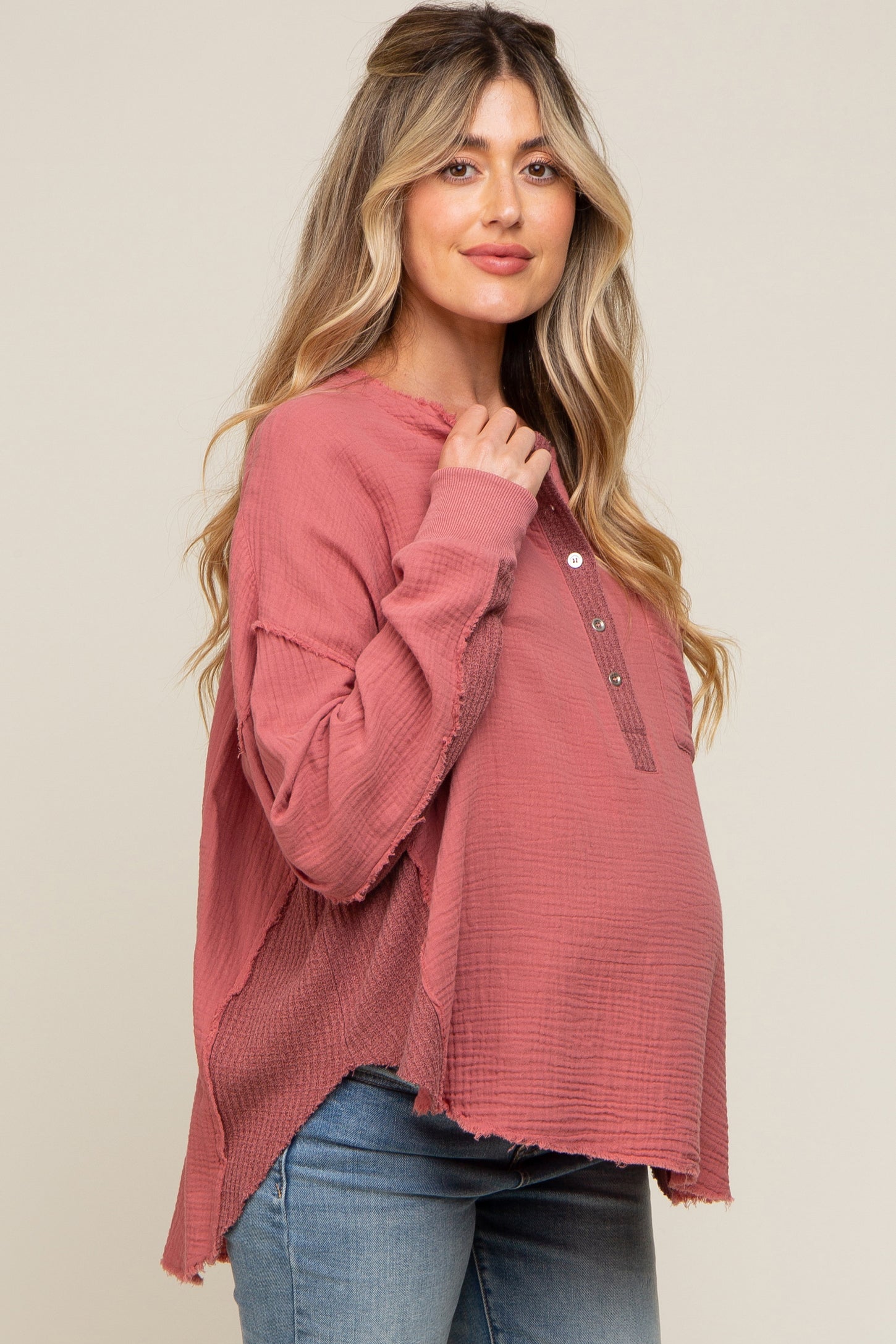 woman wearing a dusty rose maternity top with buttons and raw hem, gently cradling her baby bump