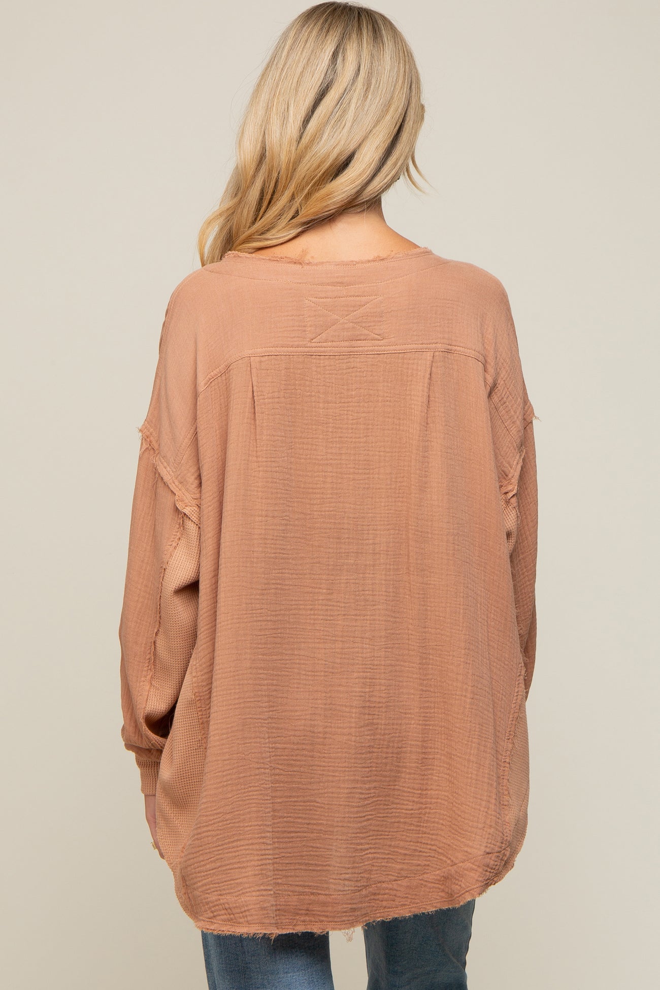 Back view of a woman wearing a mauve oversized gauze top with raw hem and waffle knit sleeves