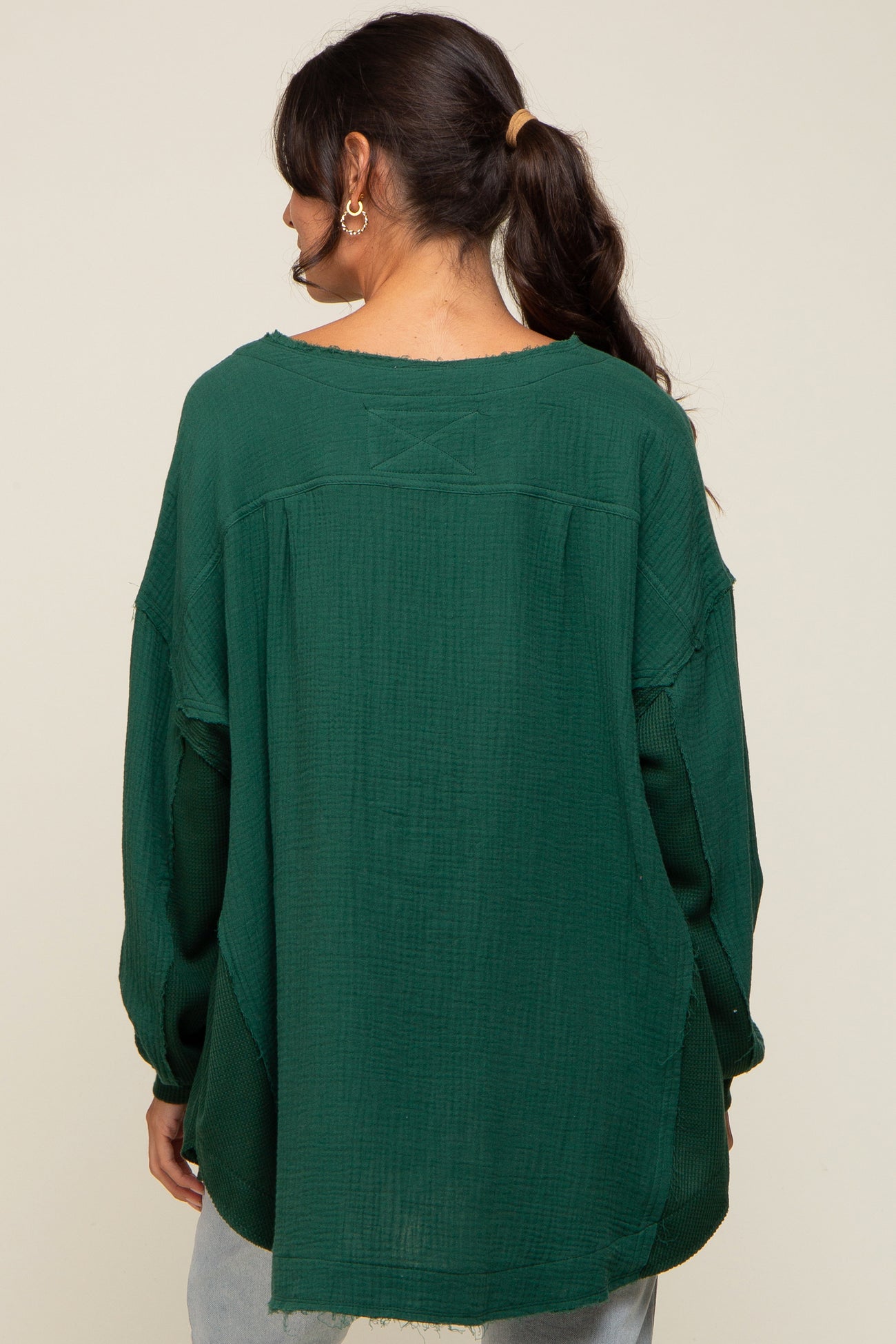 woman wearing a loose-fitting dark green textured long sleeve top, showing the back and details of the garment