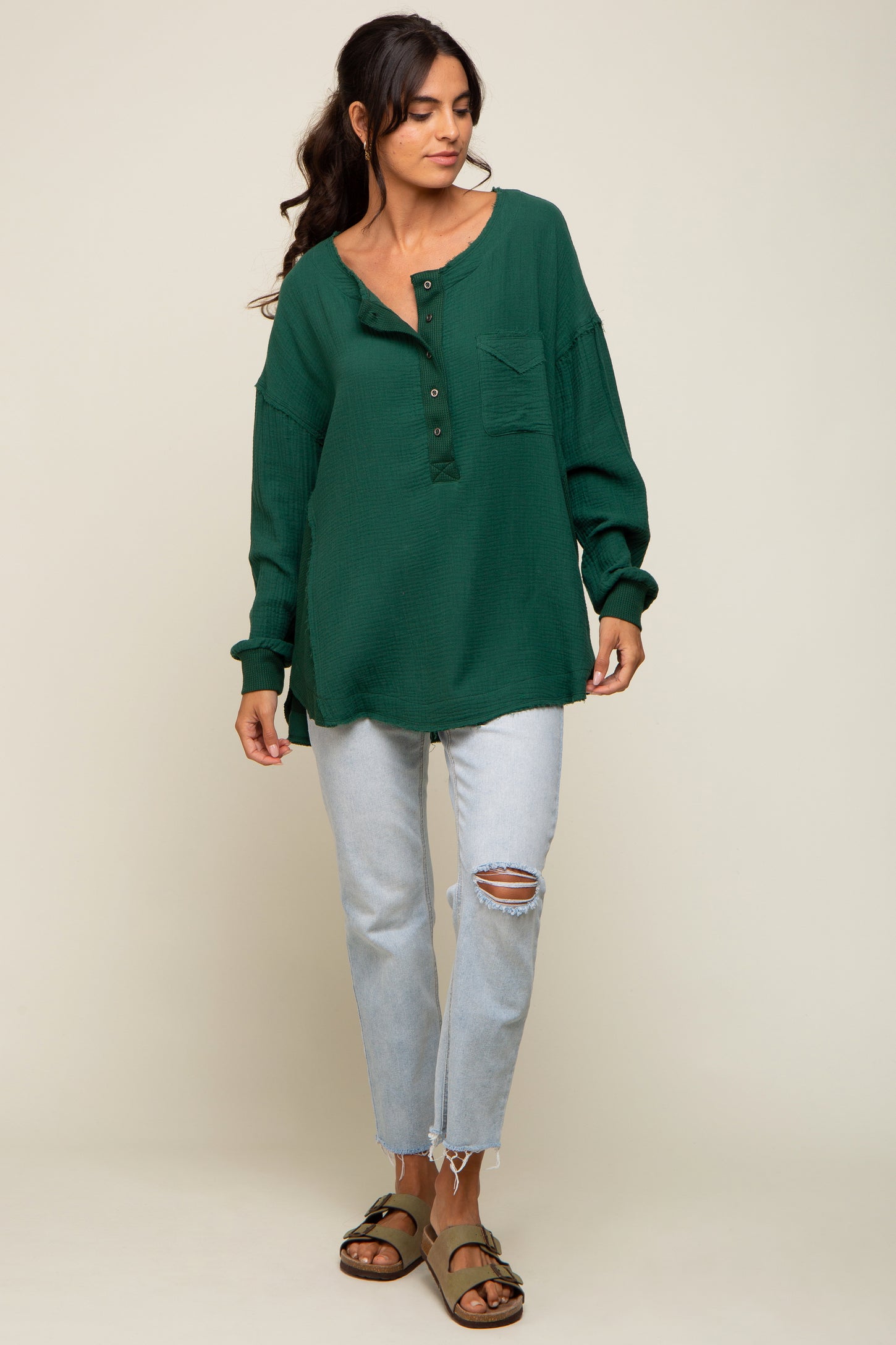 woman wearing a green waffle knit oversized henley shirt with buttons and a pocket, paired with light blue ripped jeans and sandals