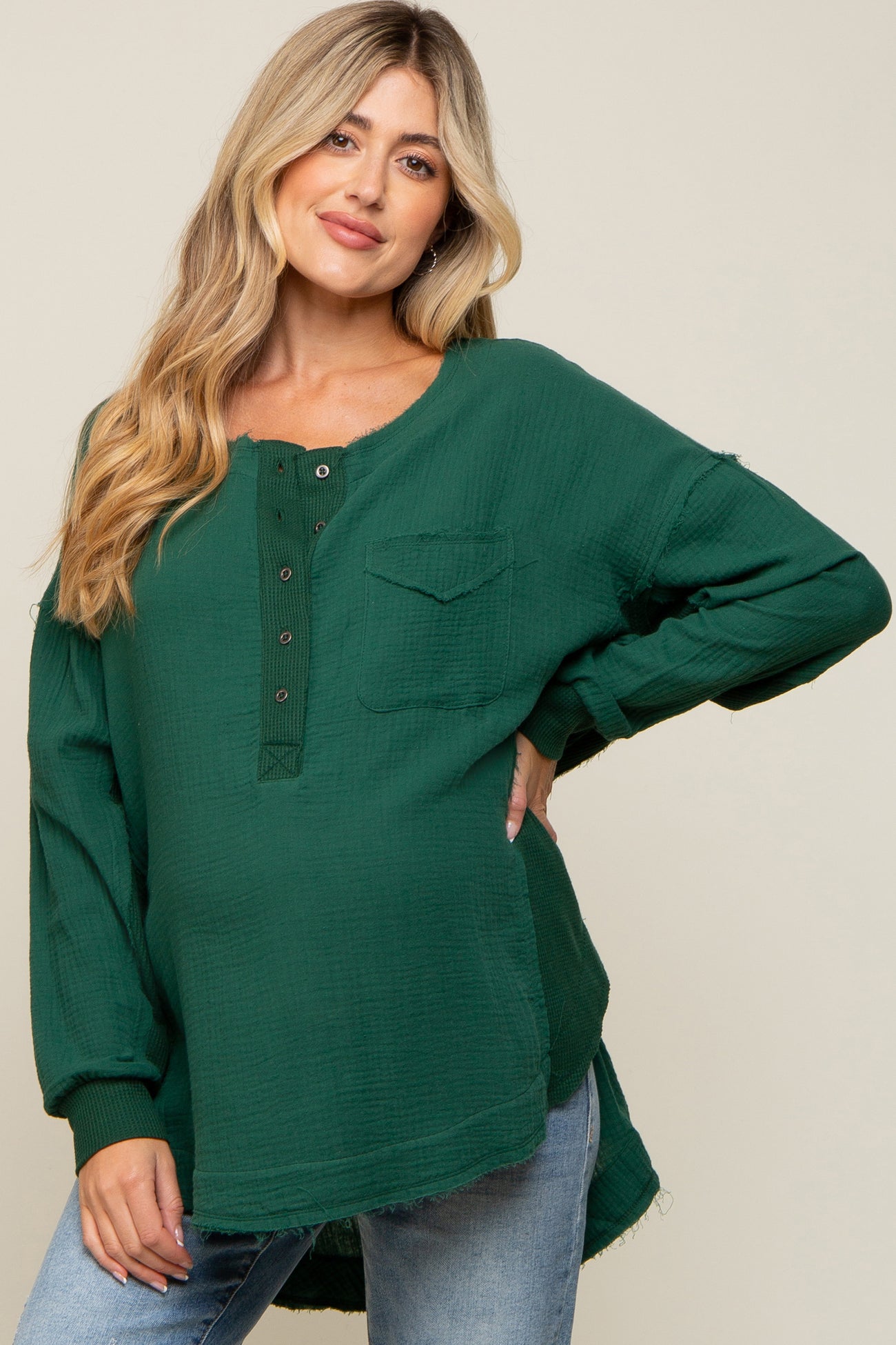 woman wearing a dark green maternity top with button details and a pocket, showcasing her baby bump