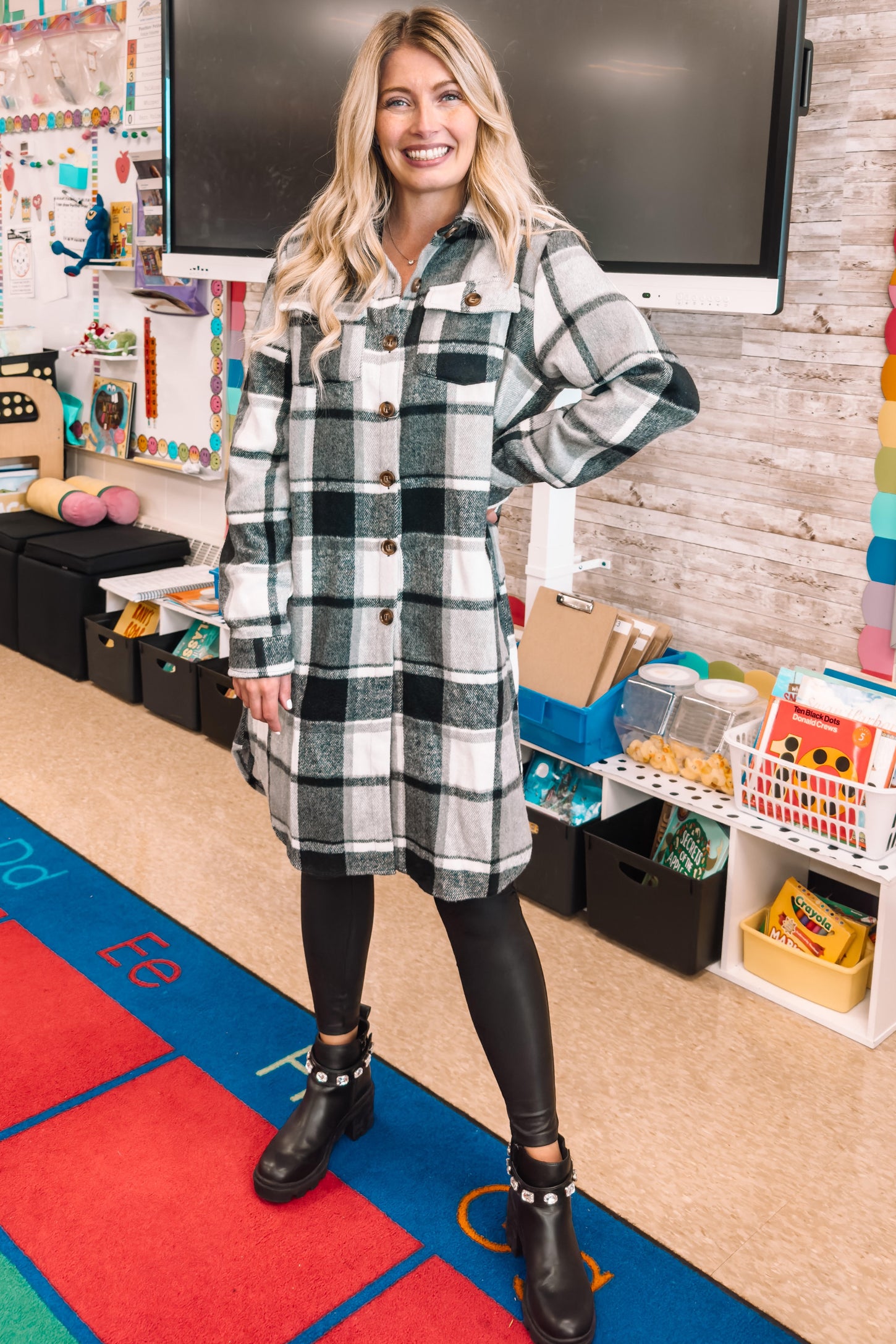 Woman wearing a long plaid shacket and black leggings standing in a colorful elementary classroom