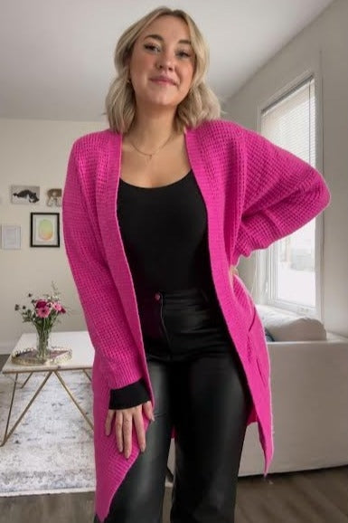 woman wearing a long bright pink waffle knit cardigan over a black top and leather pants