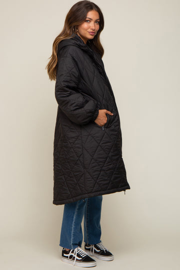 woman wearing a black quilted maternity coat with a hood, styled with jeans and sneakers