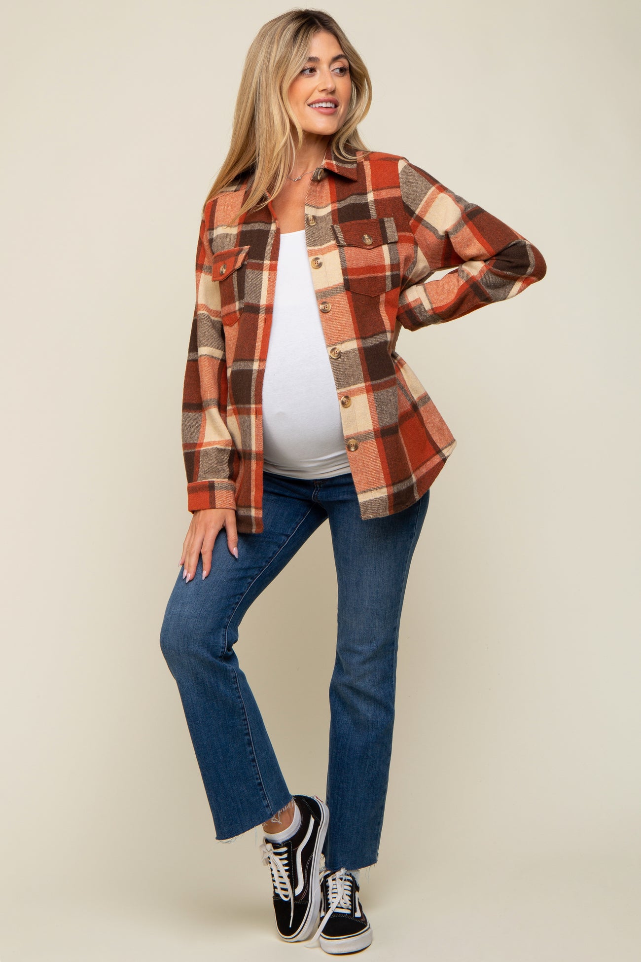 woman wearing a red and orange plaid maternity shacket over a white top, posing with her baby bump visible and paired with jeans and sneakers