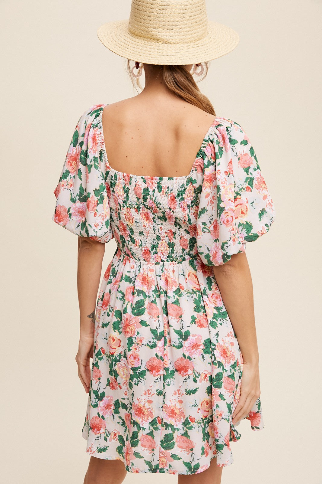 woman wearing a floral short dress with puff sleeves and a smocked back, styled with a straw hat