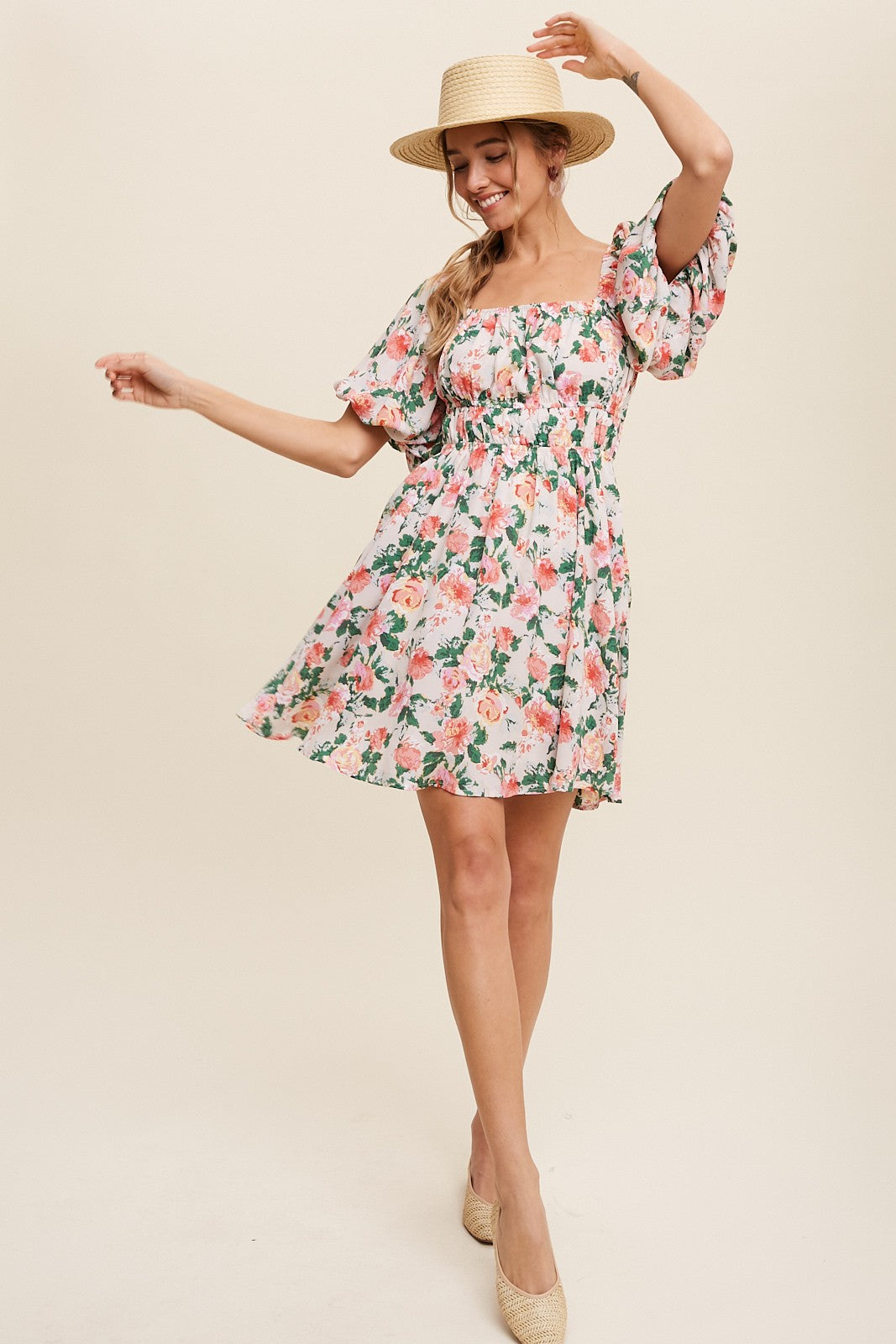 woman wearing a floral pink short dress with puff sleeves and a straw hat, twirling playfully