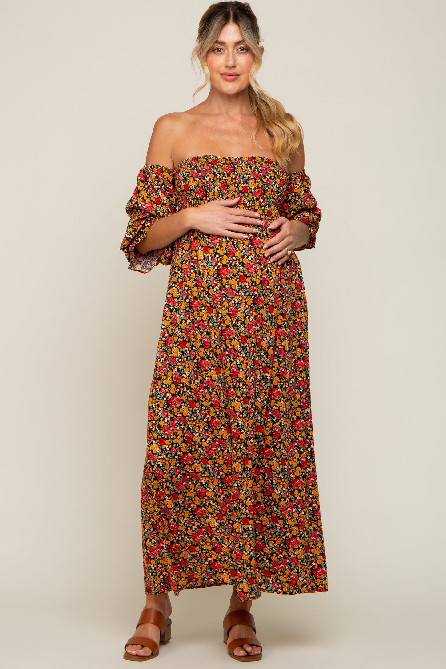 woman wearing a black floral off-the-shoulder maternity maxi dress and holding her baby bump