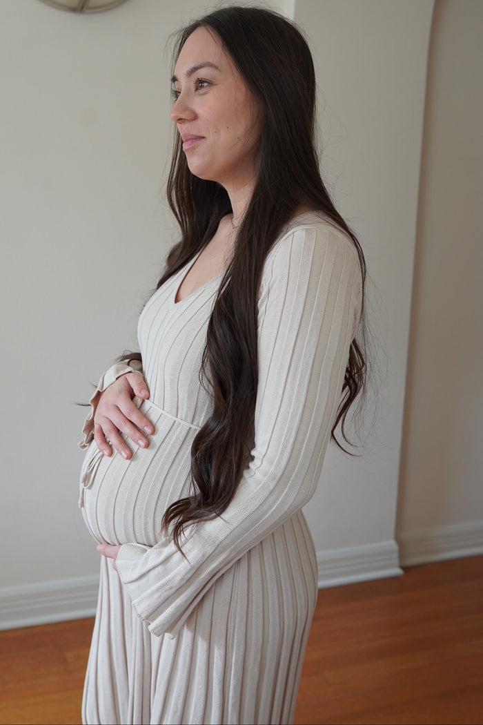 woman wearing a beige ribbed maternity dress and holding her baby bump