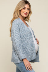 woman wearing a light blue knitted maternity cardigan and holding her baby bump