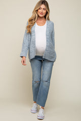 woman wearing a light blue knitted maternity cardigan over a white tank top and ripped jeans, showing her baby bump