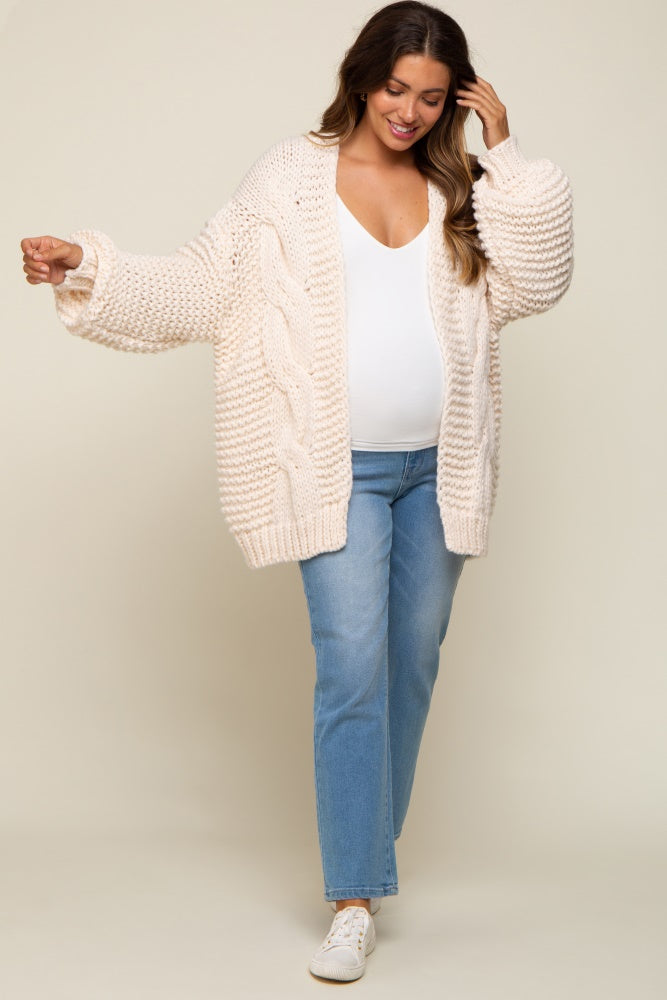 woman wearing a cream oversized knitted maternity cardigan over a white top and blue jeans, showcasing her baby bump