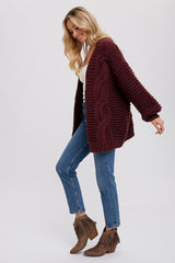 woman wearing a burgundy oversized knitted cardigan with cable knit details, paired with blue jeans and brown fringe ankle boots