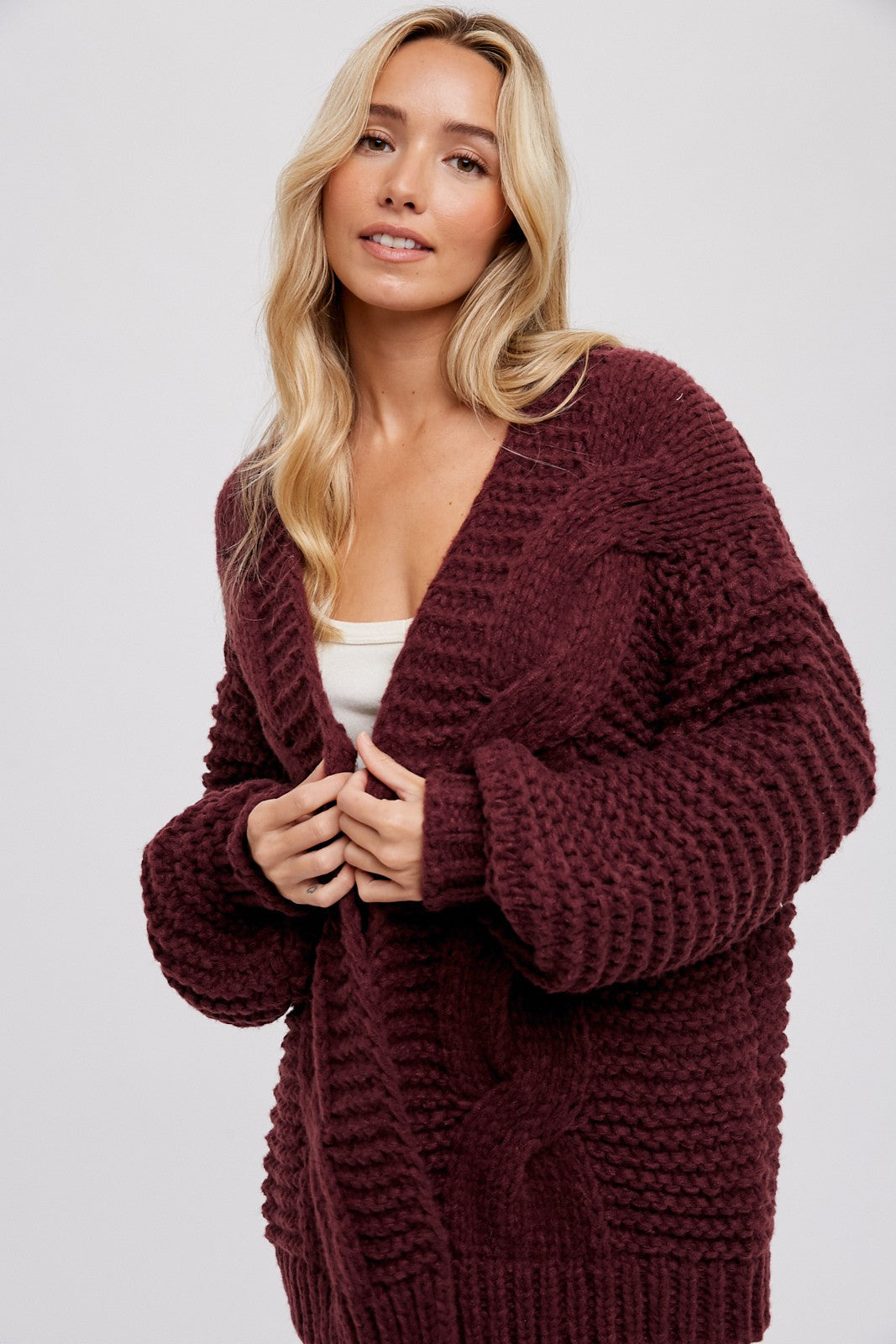 woman wearing a burgundy chunky cable knit cardigan with oversized sleeves and an open front
