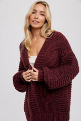 woman wearing a burgundy chunky cable knit cardigan with oversized sleeves and an open front
