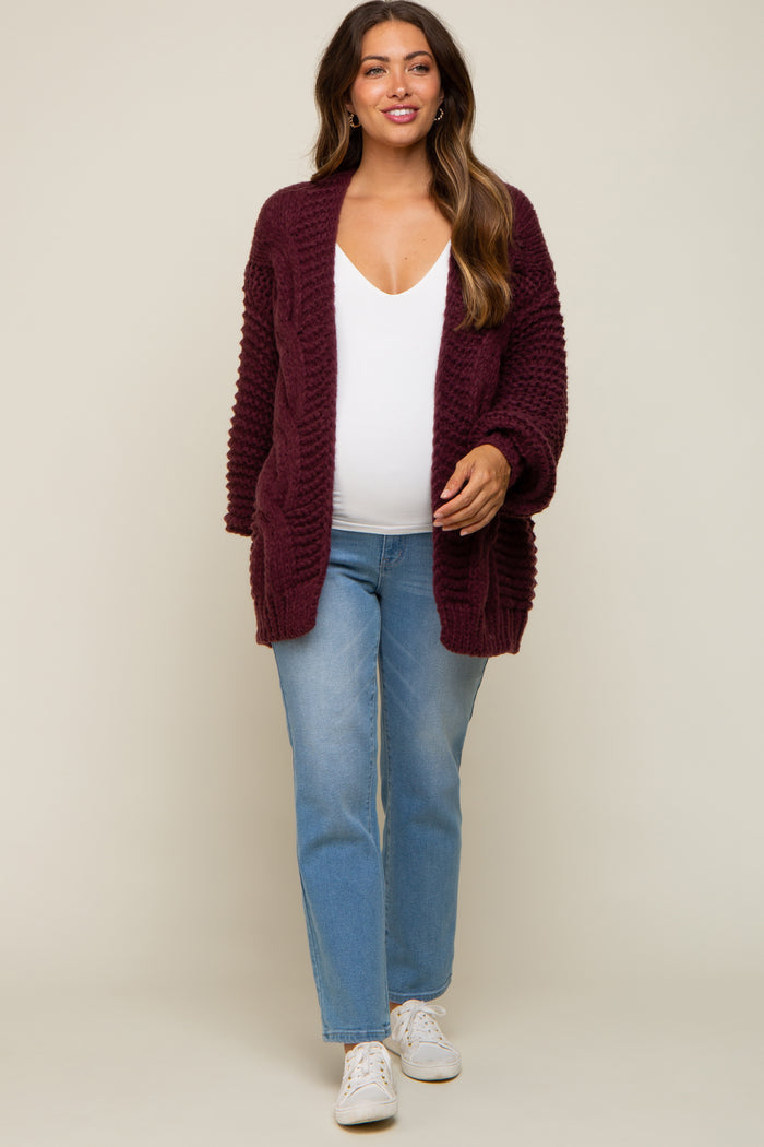 woman wearing a burgundy maternity cardigan over a white top and blue jeans, showing her baby bump