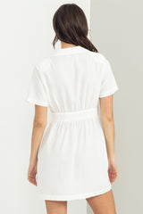 woman wearing a white short sleeve dress with a belted waist and a collared neckline, shown from the back