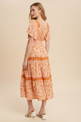 woman wearing a pink floral midi dress with short sleeves and a tiered skirt, showing the back view