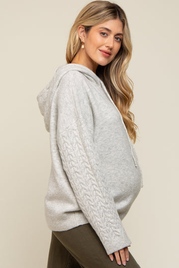 woman wearing a light gray maternity hoodie with cable knit sleeves, showing her baby bump