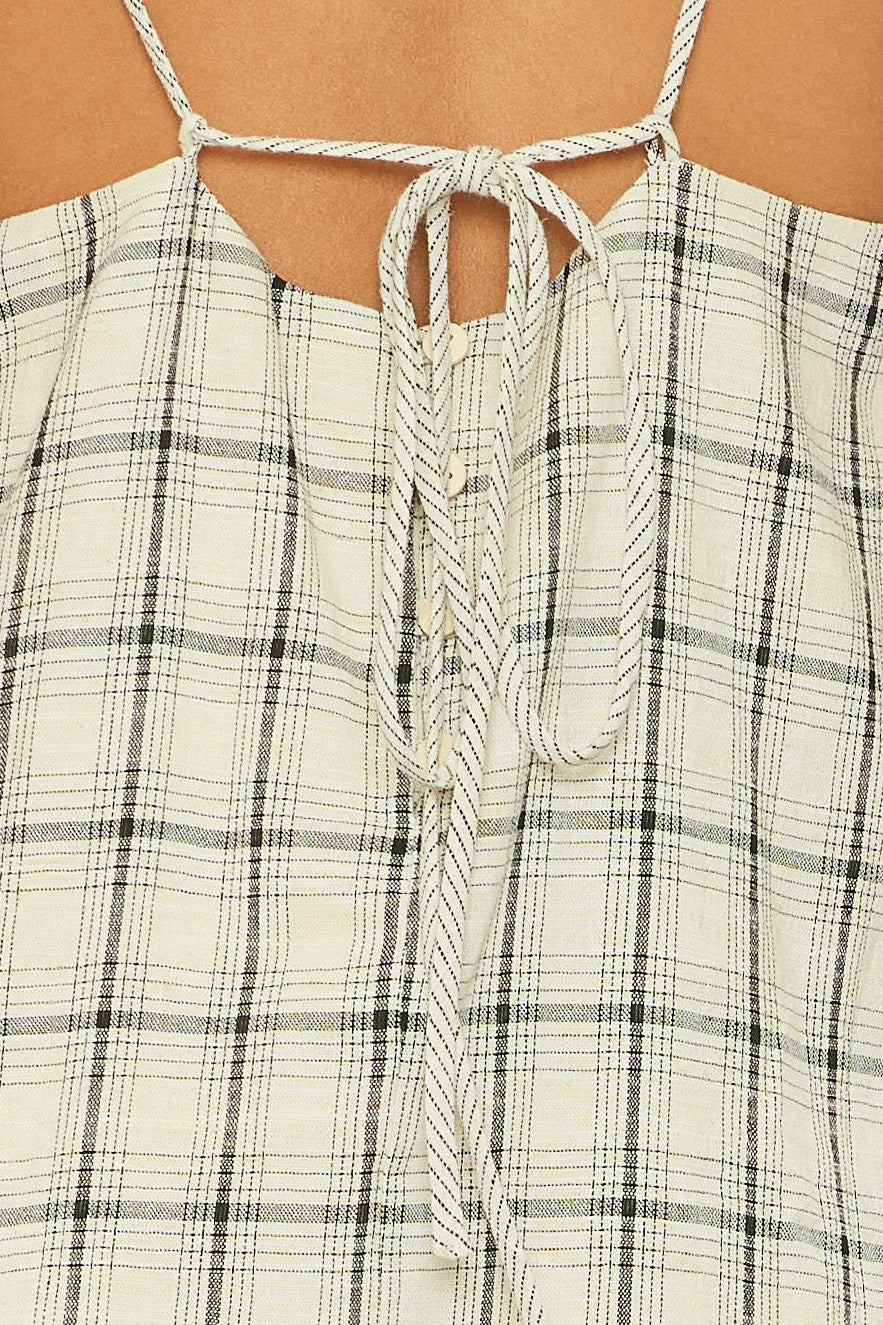 woman wearing a light plaid sleeveless top with adjustable tie straps and button details at the center