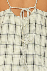 woman wearing a light plaid sleeveless top with adjustable tie straps and button details at the center